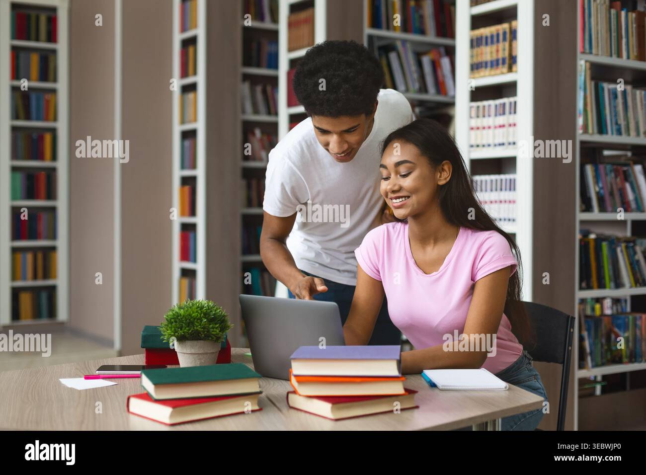 Students Collaborating Together in a Library While Using a Laptop and Studying Stock Photo