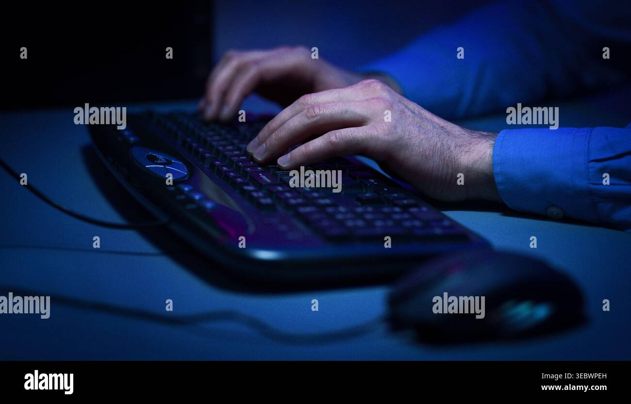 Hands Typing on a Keyboard in a Low Light Setting During Late Night Work Stock Photo