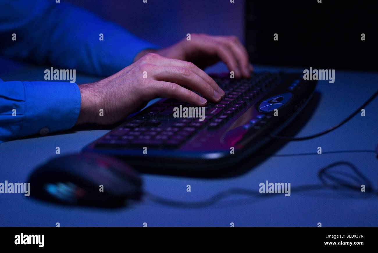 Hands Typing on a Keyboard in a Dimly Lit Room While Using a Computer Stock Photo