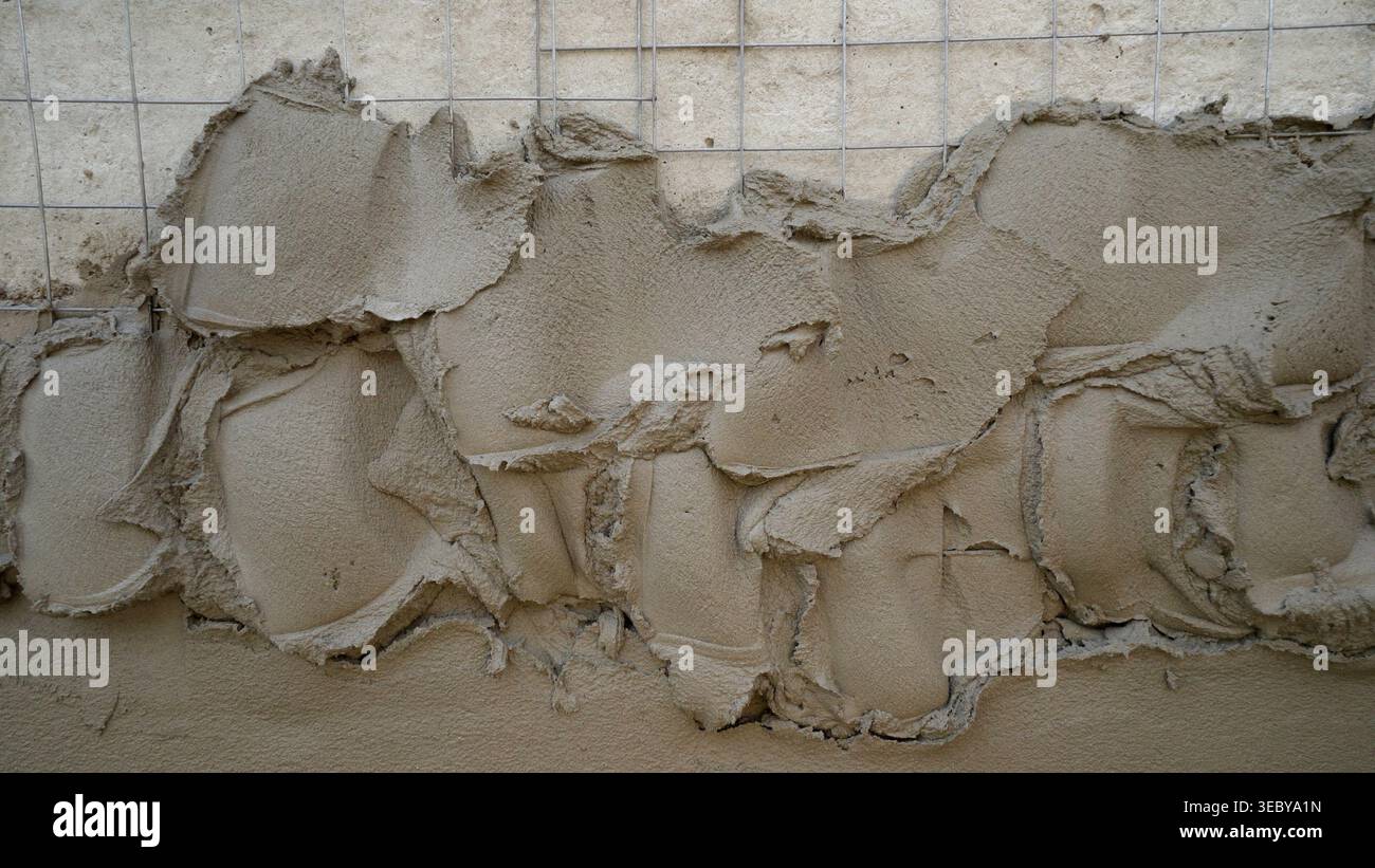 Plastering process on a wall using a metal mesh and cement mixture, creating a textured surface for building construction Stock Photo