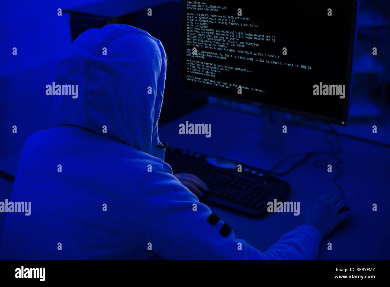 Person Working on Computer in Dimly Lit Room With Blue Lighting and Code on Screen Stock Photo