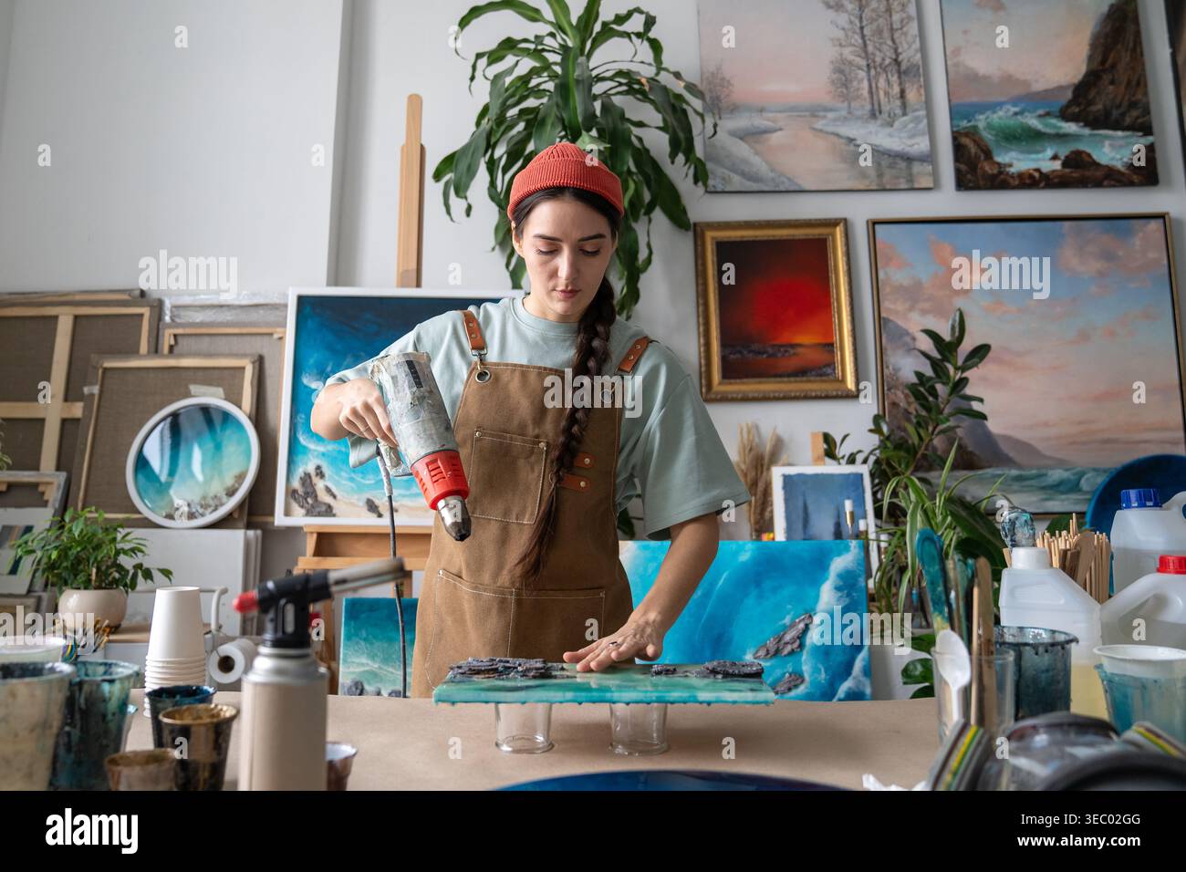 Concentrated woman designer working on epoxy resin painting at worktable in home art studio. Stock Photo