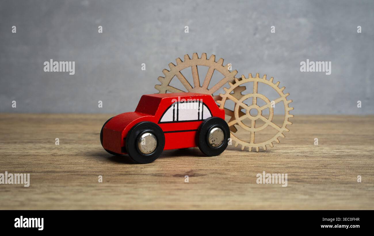 Red toy car with wooden gears in the background representing automotive engineering and mechanics. Stock Photo