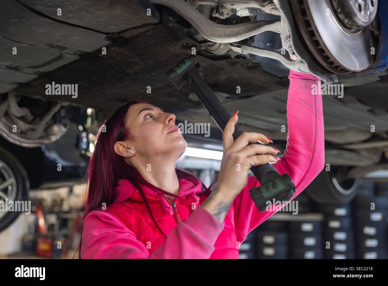 Female mechanic inspecting the underside of a vehicle, diagnosing ...