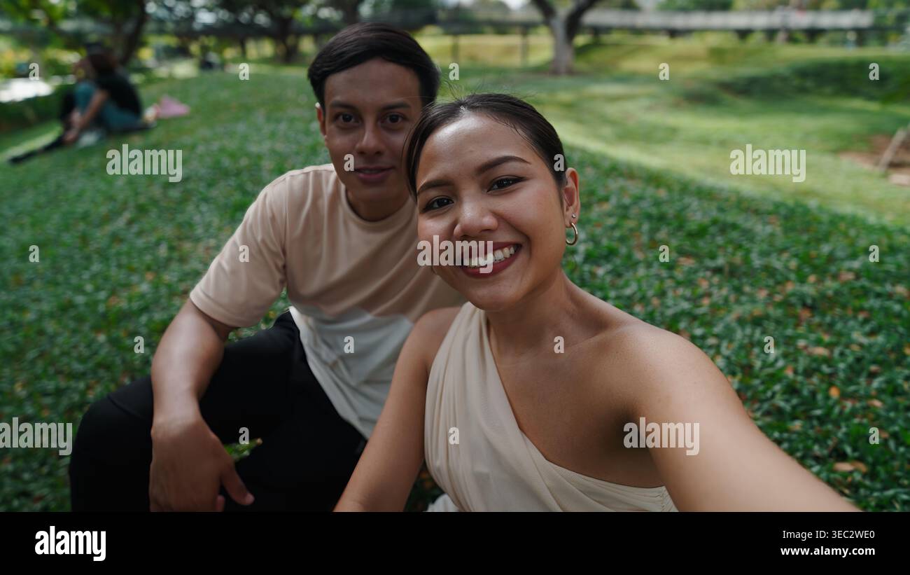 Young couple taking selfie, smiling during outdoor park leisure moment Stock Photo