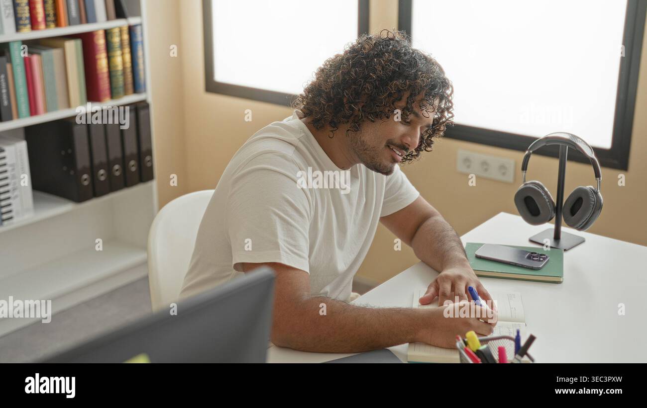 Man writing in notebook at desk in a library building, pen to lips thinking gesture; focused study and learning. Stock Photo