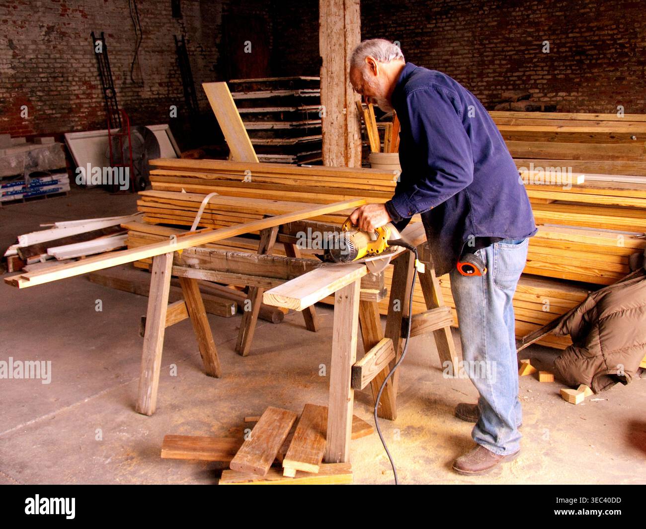 White male senior volunteer at Habitat for Humanity's Restore, cutting lumber with an electric circular saw, New Orleans, LA.  MR Stock Photo