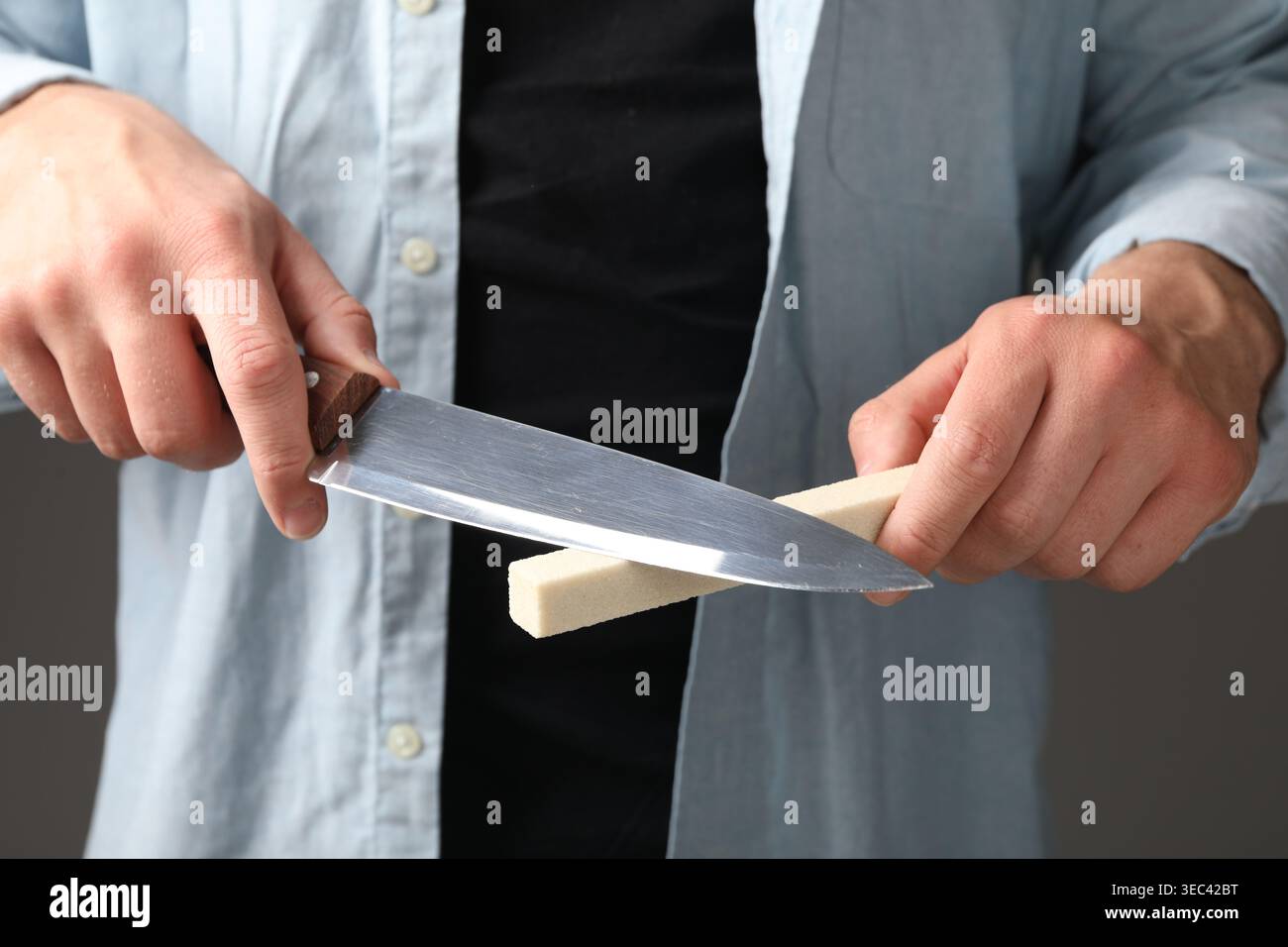 Man sharpening knife on grey background, closeup Stock Photo