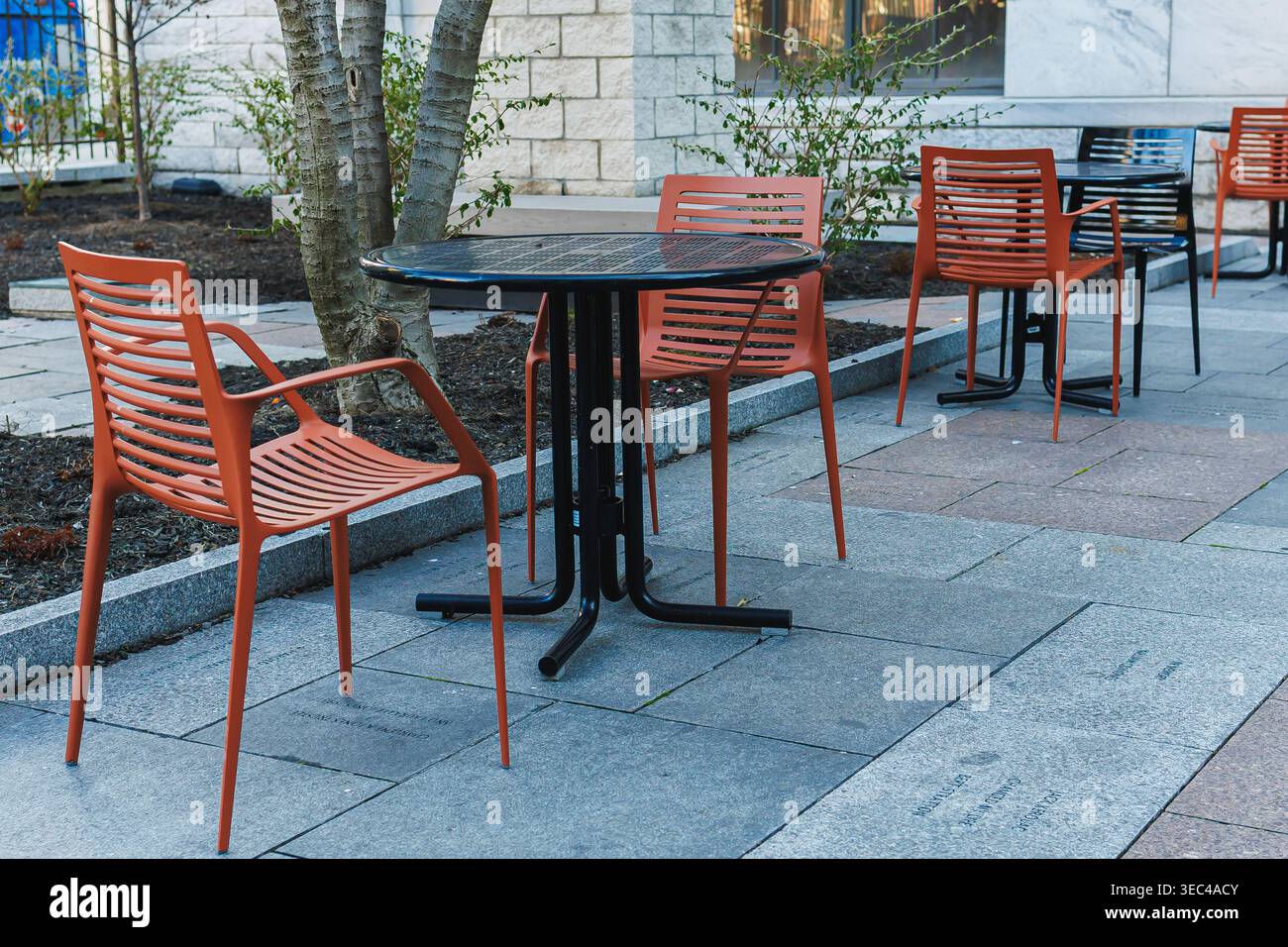 Outdoor seating area with red chairs and a black table near a building during daylight in an urban space Stock Photo