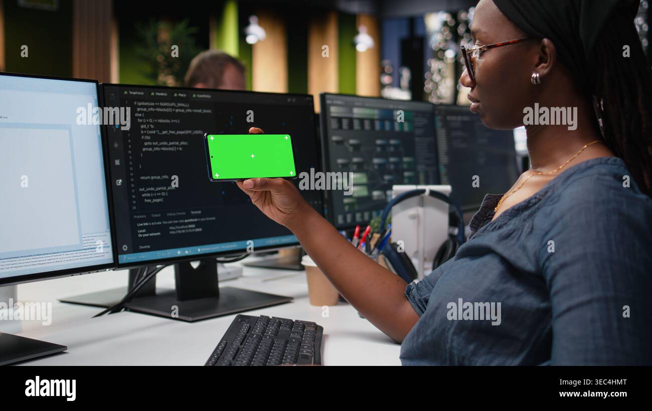 Green screen phone used by woman in company workplace doing tech quality assurance. Woman in office watches tutorial on programming languages with chroma key smartphone Stock Photo