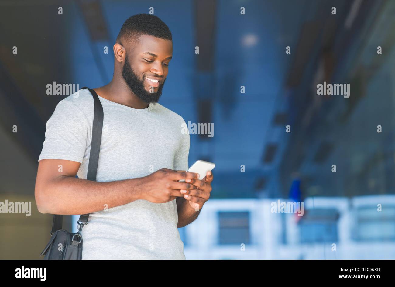 Young Man Smiles While Using Smartphone in Modern Urban Environment Stock Photo