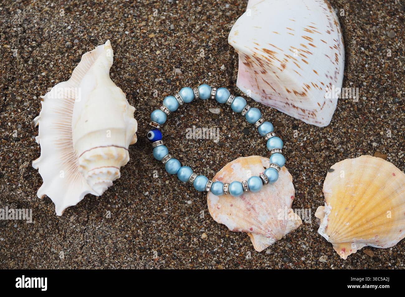 Beads placed among seashells on sandy beach Stock Photo