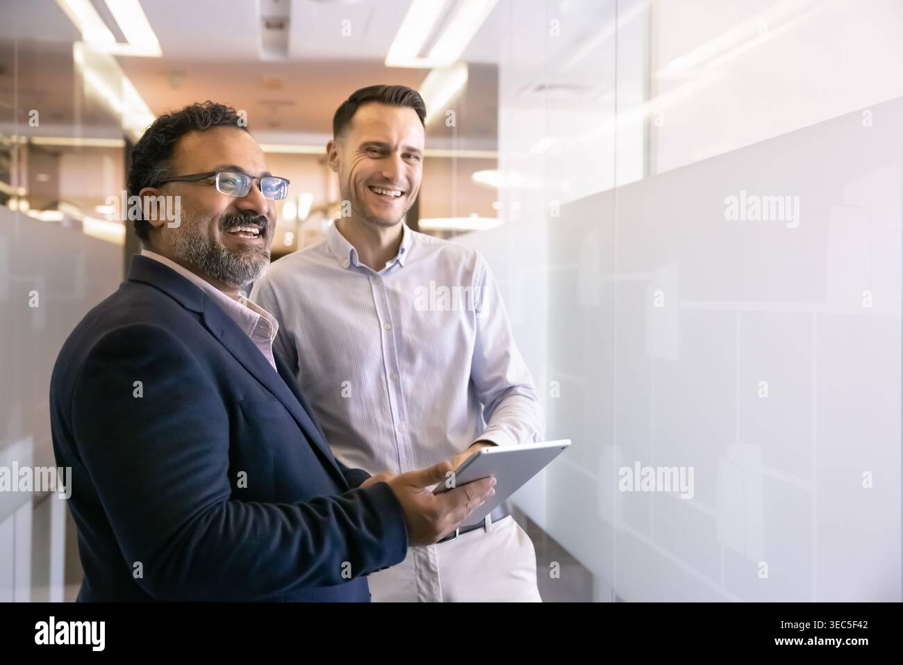 Two happy multiethnic team members standing together in office hallway Stock Photo