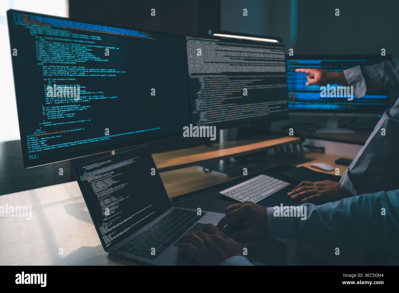 man programmer writing program code at a multi monitor workstation with laptop and software code on screens, performing debugging, software developmen Stock Photo