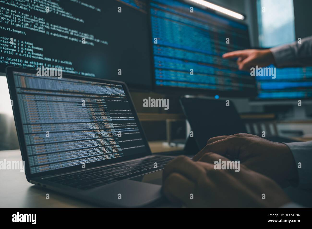 Developer programming code at a multi monitor workstation with laptop and screens displaying scripts, showing software development workflow, coding pr Stock Photo