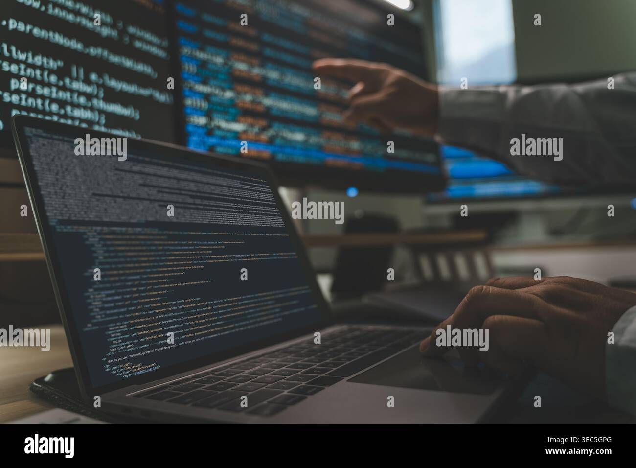 Developer programming code at a multi monitor workstation with laptop and screens displaying scripts, showing software development workflow, coding pr Stock Photo