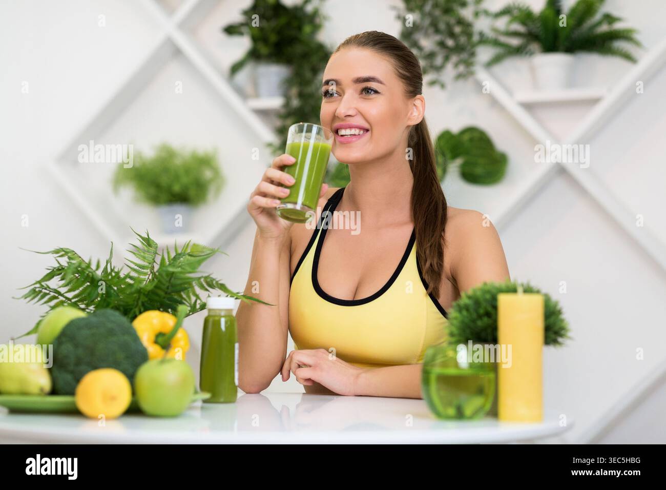 Woman Enjoying a Green Smoothie in a Healthy Kitchen Surrounded by Fresh Fruits and Vegetables Stock Photo