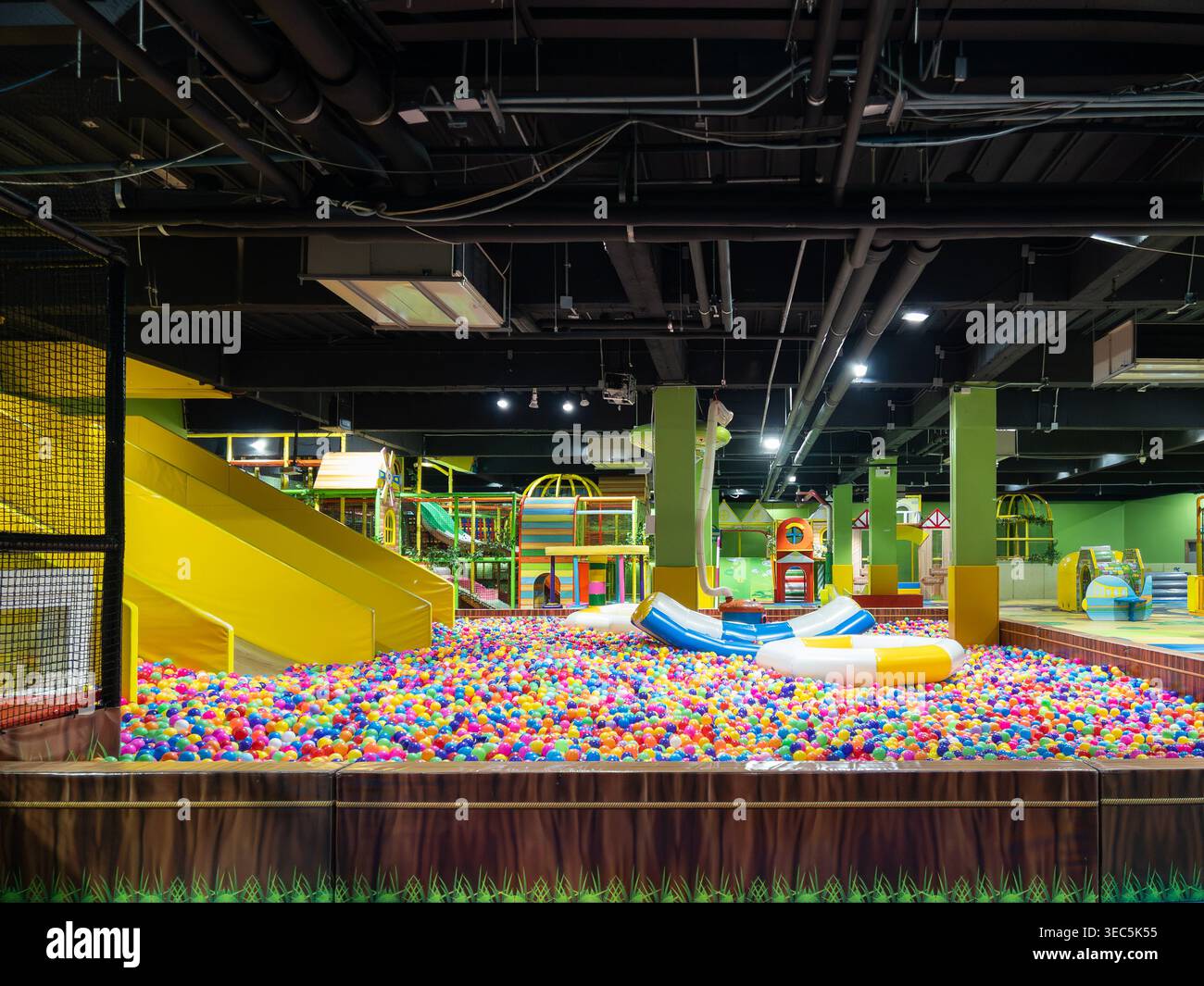A vibrant indoor playground featuring a large multi-colored ball pit, yellow slides, and various play structures designed for children's recreation an Stock Photo