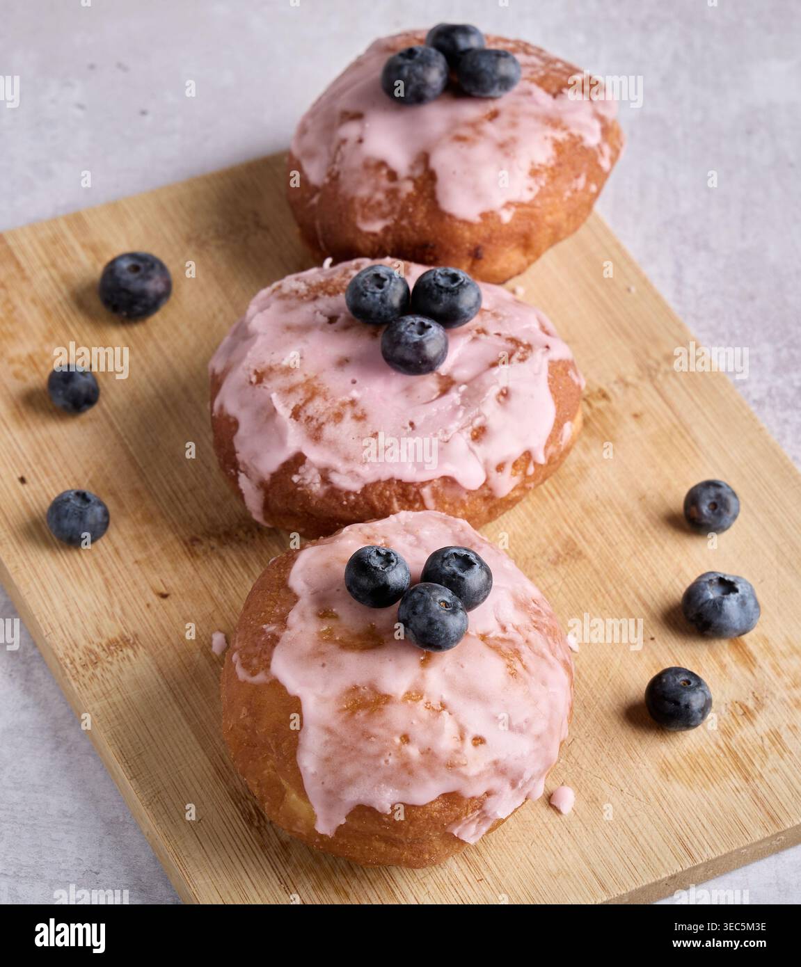 Pink Glazed Donuts with Fresh Blueberries on Board Stock Photo