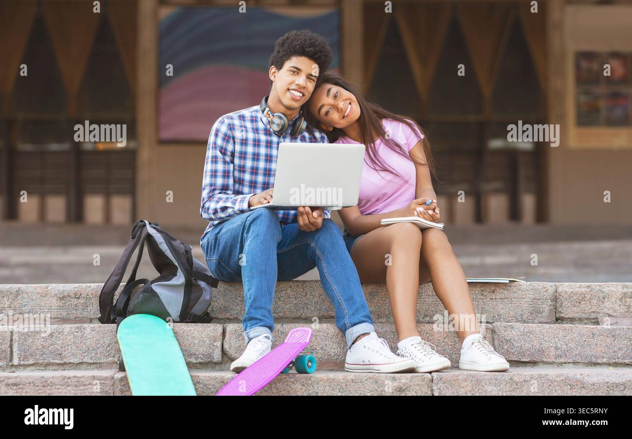 Young Couple Studying Together on Steps With Laptops and Skateboards at School Stock Photo