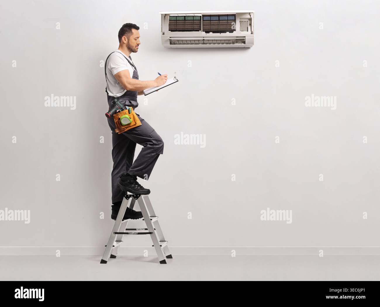 Technician on a ladder checking an air conditioning unit on a wall Stock Photo