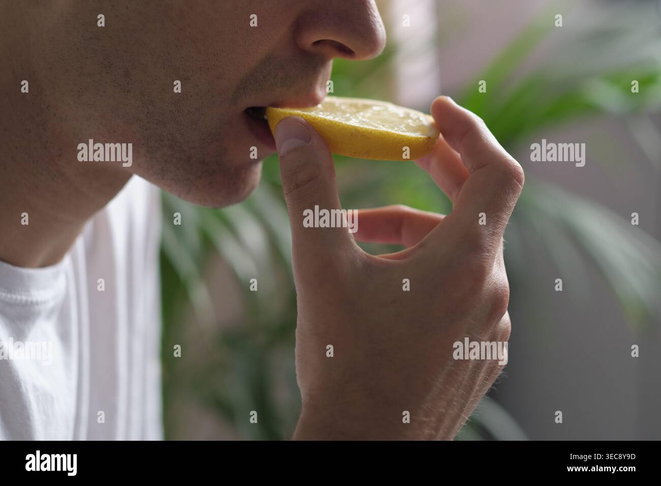 A man touches a lemon slice with his lips, exploring its sourness. The scene suggests detox rituals, natural energy, and the rediscovery of taste Stock Photo