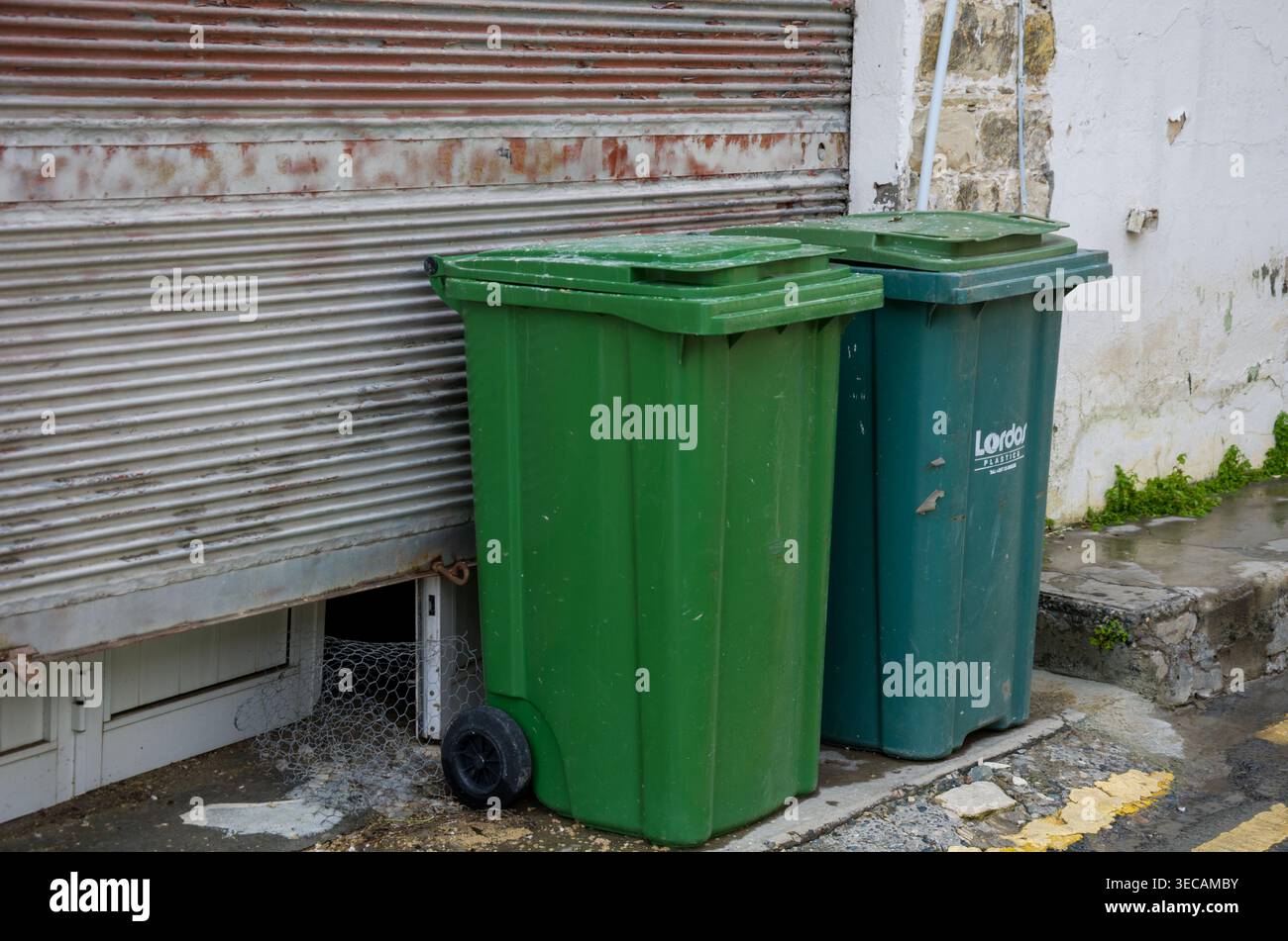 Two green garbage bins beside a weathered wall Stock Photo