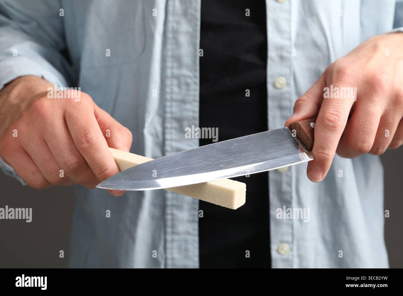 Man sharpening knife on grey background, closeup Stock Photo