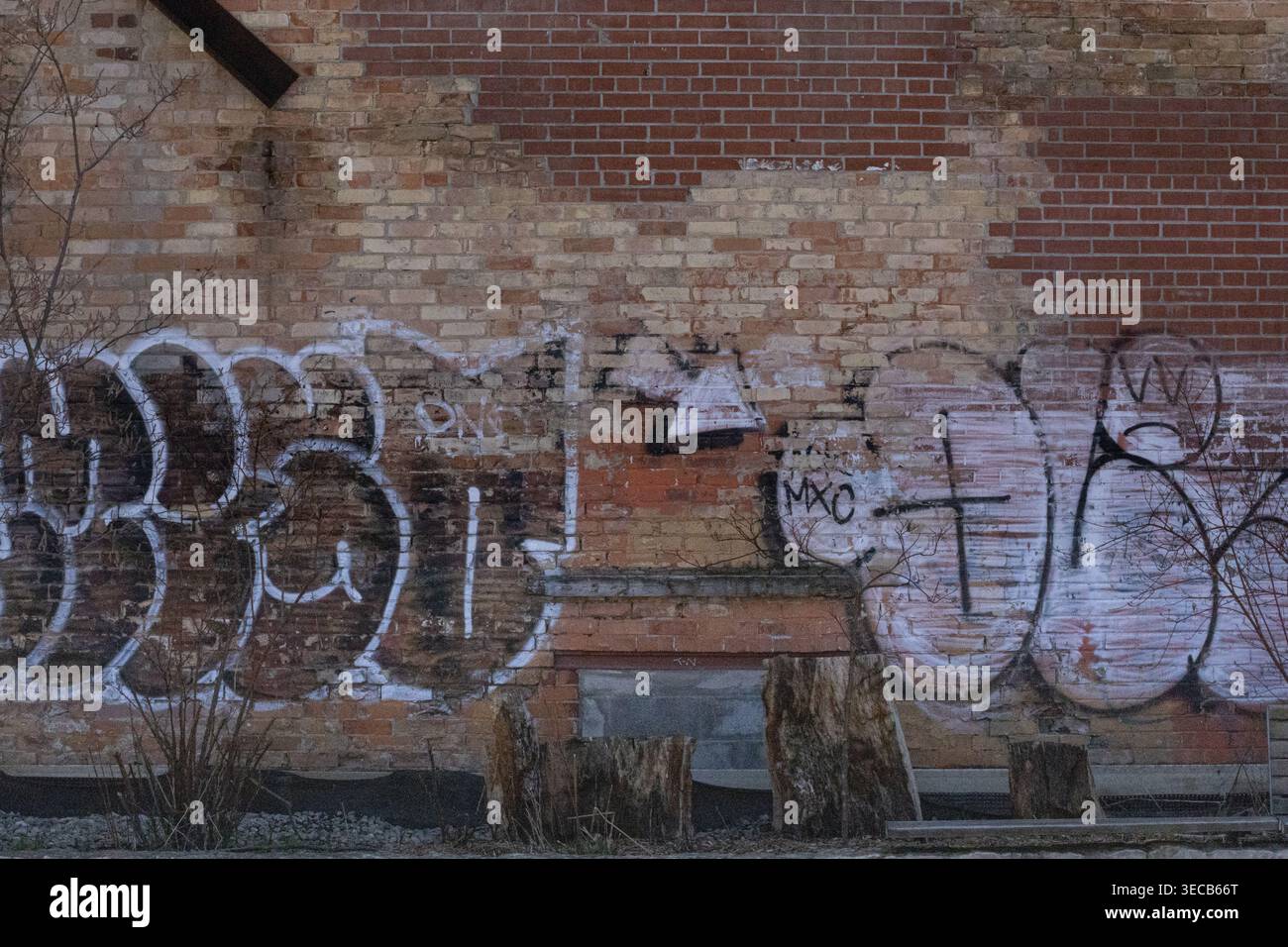 Aged red brick wall with patchwork repairs and graffiti in white and black paint, showing worn urban texture and weathered surface. Stock Photo