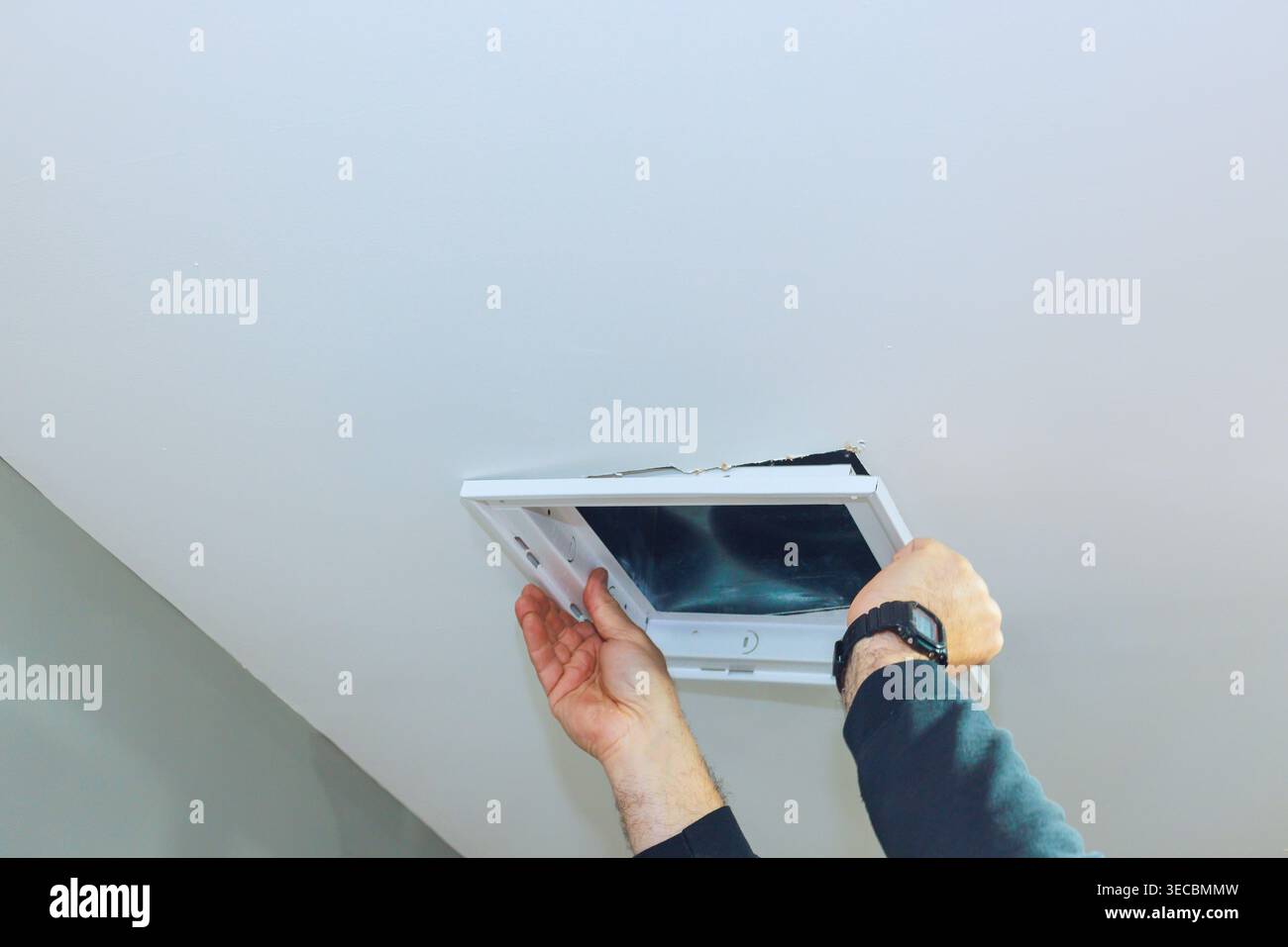 Contractor is taking off an access ceiling vent panel from ceiling while standing in room. Stock Photo