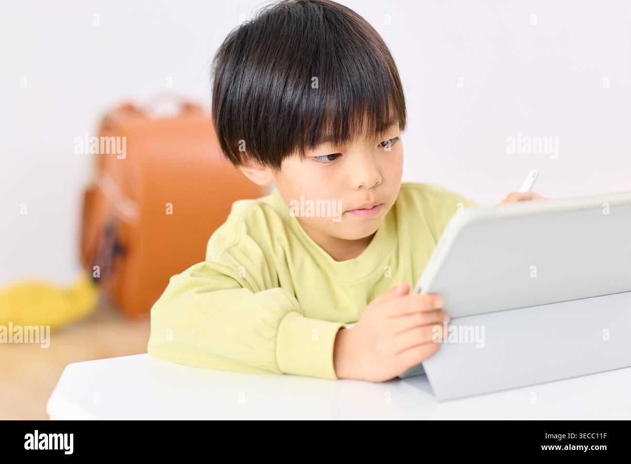 Japanese elementary school boy focused on tablet learning at home Stock Photo