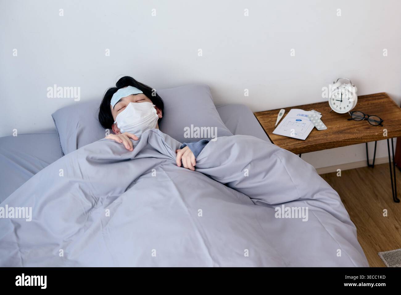 Sick Japanese young man resting in bed with mask and cooling sheet Stock Photo