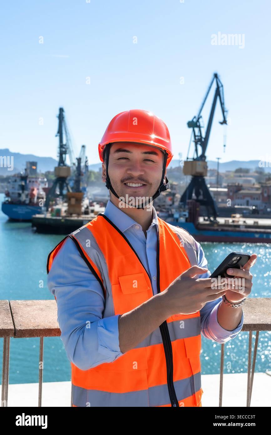 Port worker smiling while using a smartphone Stock Photo