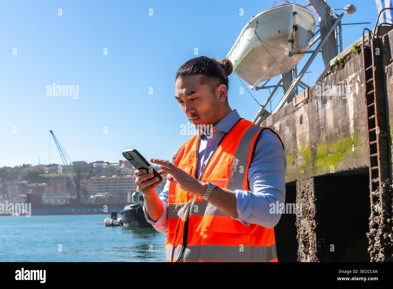 Asian cargo port worker using smartphone for logistics management Stock Photo