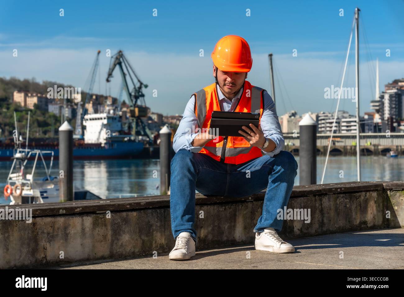 Port worker wearing safety vest checking tablet at harbor Stock Photo