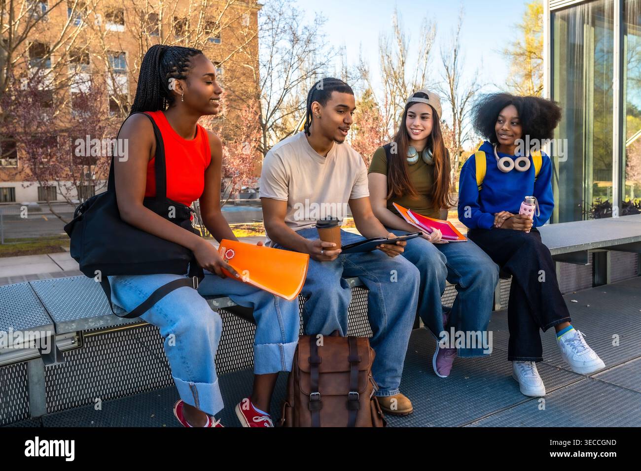Diverse students talking on university campus bench Stock Photo
