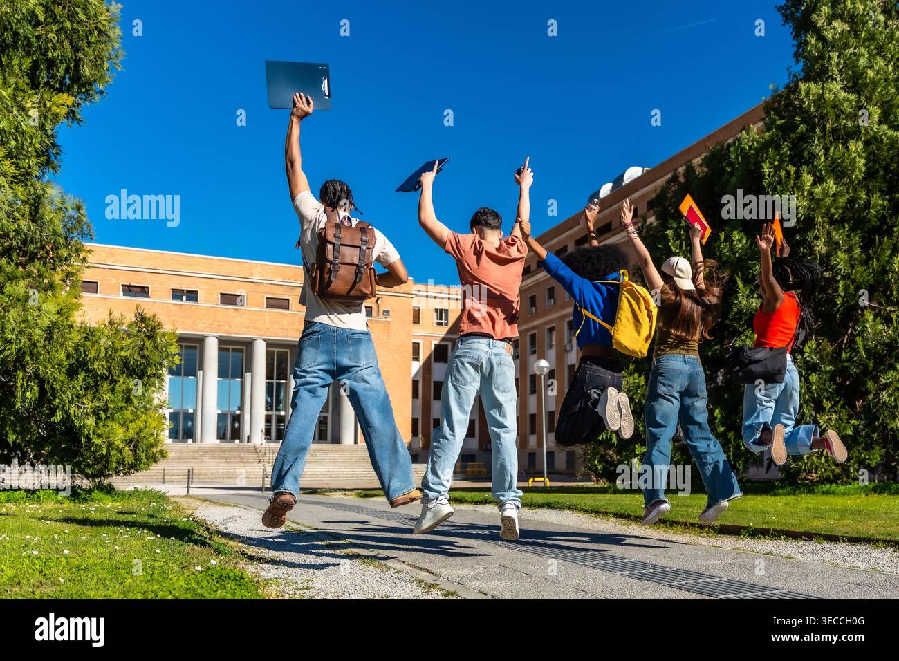 Diverse students jumping celebrating success on university campus Stock Photo