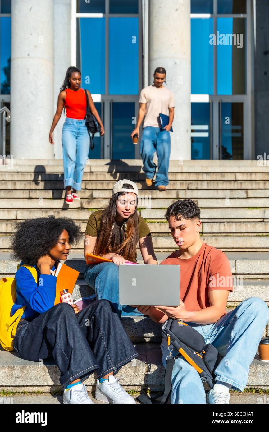 Diverse students collaborating on laptop on campus stairs Stock Photo