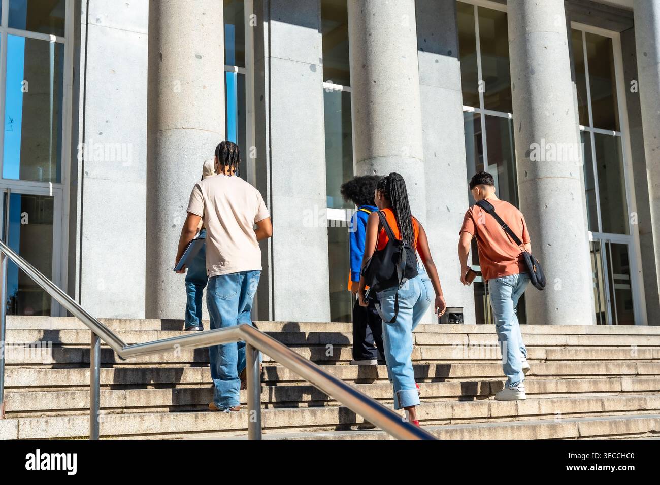 Diverse students walking up stairs on university campus Stock Photo