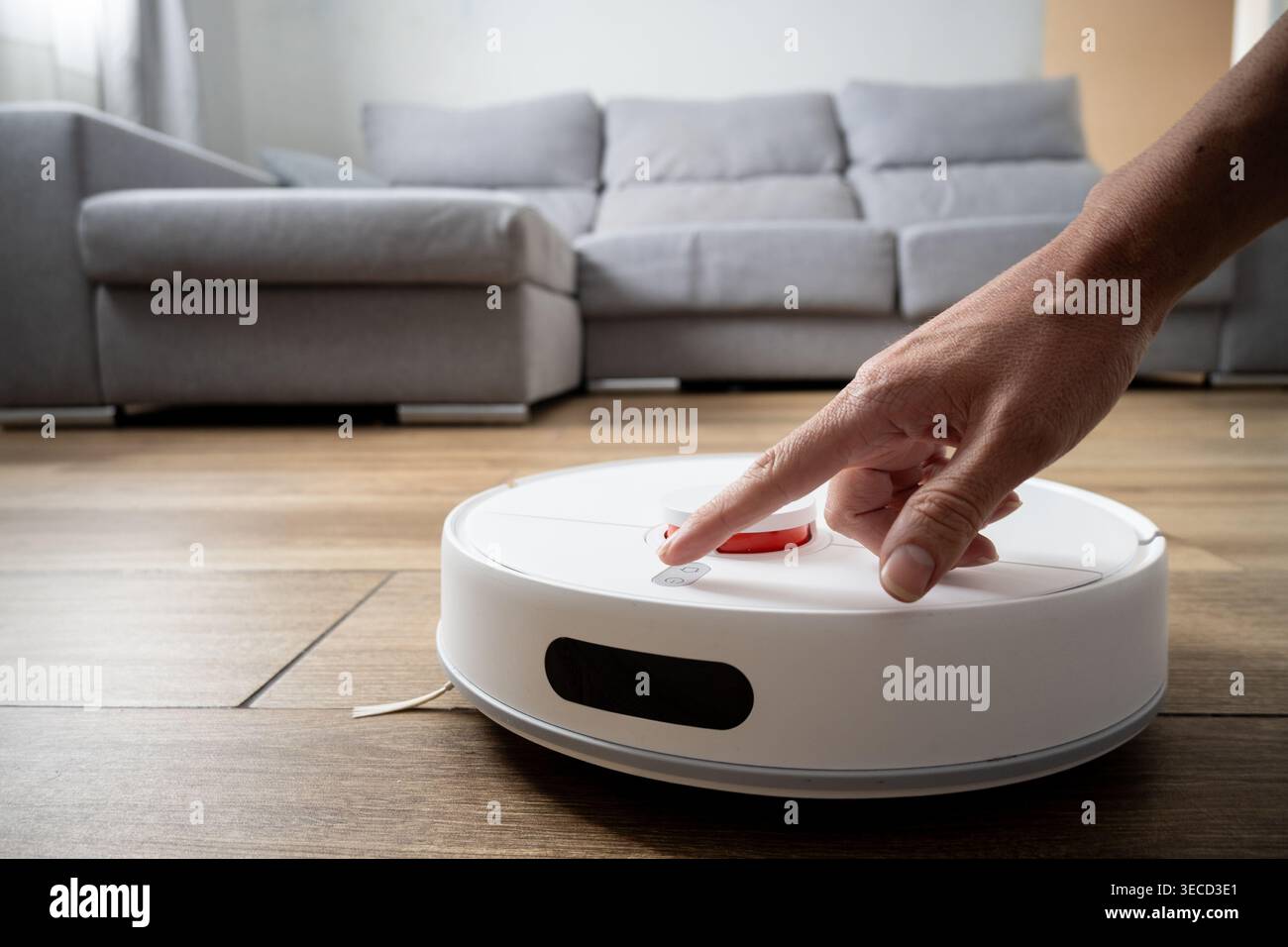 Close-up of a hand pressing the control button on a smart robot vacuum cleaner on a wooden floor. Concept of home automation, smart technology, user i Stock Photo