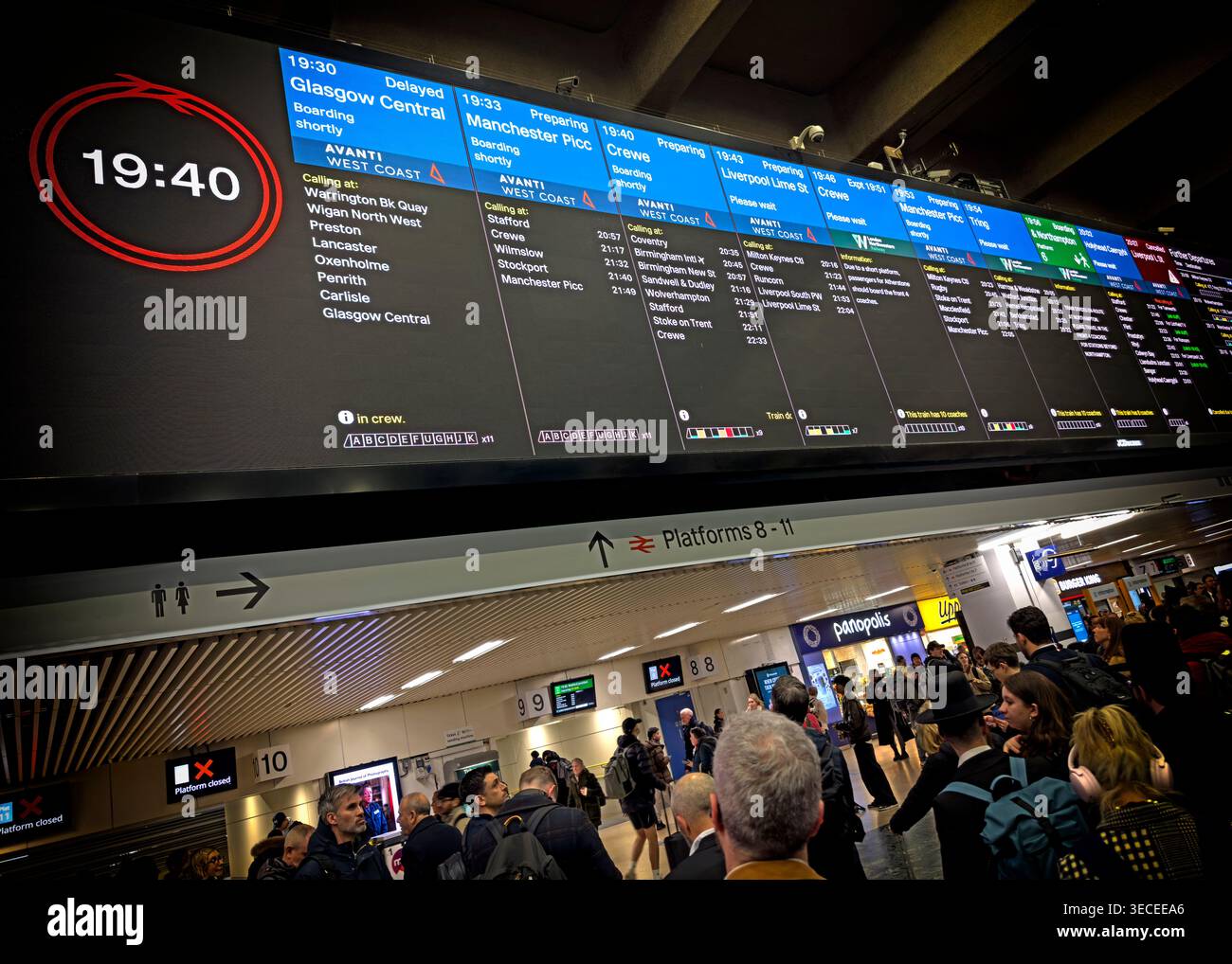 Passengers wait below Euston station departure boards at evening peak, with northbound trains delayed and few services ready to board. Stock Photo