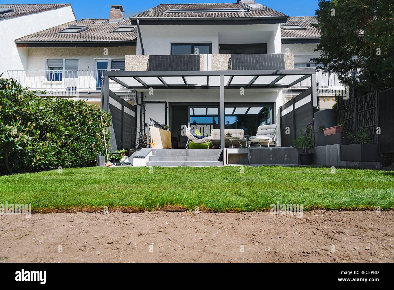 Gardening. Making a lawn from a roll. Green grass texture - well-groomed turf in the garden with a modern house in the background. Stock Photo