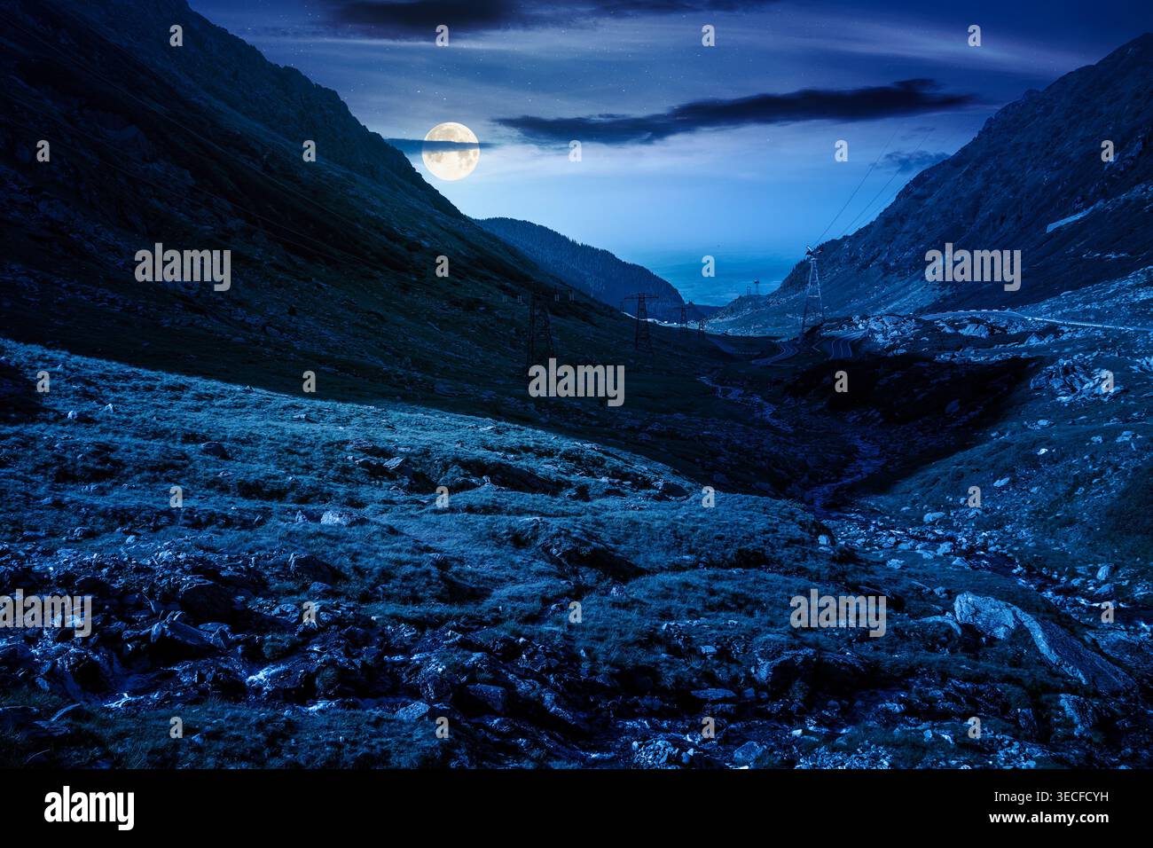 road through mountains winding uphill at night. full moon over popular highway travel destination of Romania. mysterious view of mountain on summertim Stock Photo