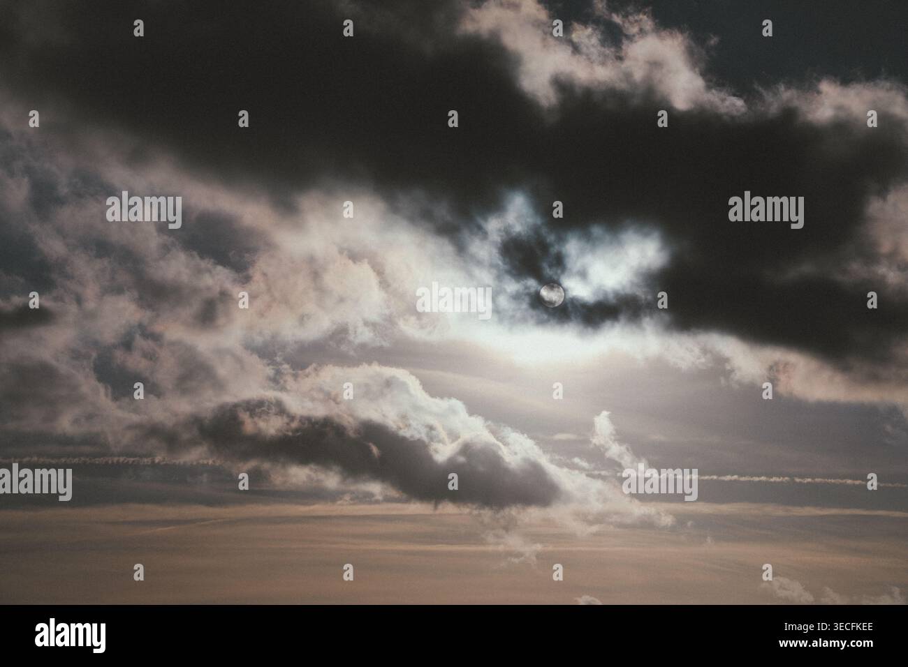 Dramatic cloudy sky with sun partially hidden behind dark storm clouds. Stock Photo