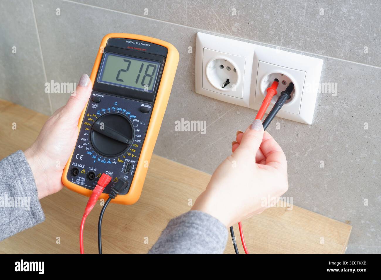 Woman with a multimeter check the voltage of the electrical network. Close-up view of the hands with the appliance near the socket. Stock Photo