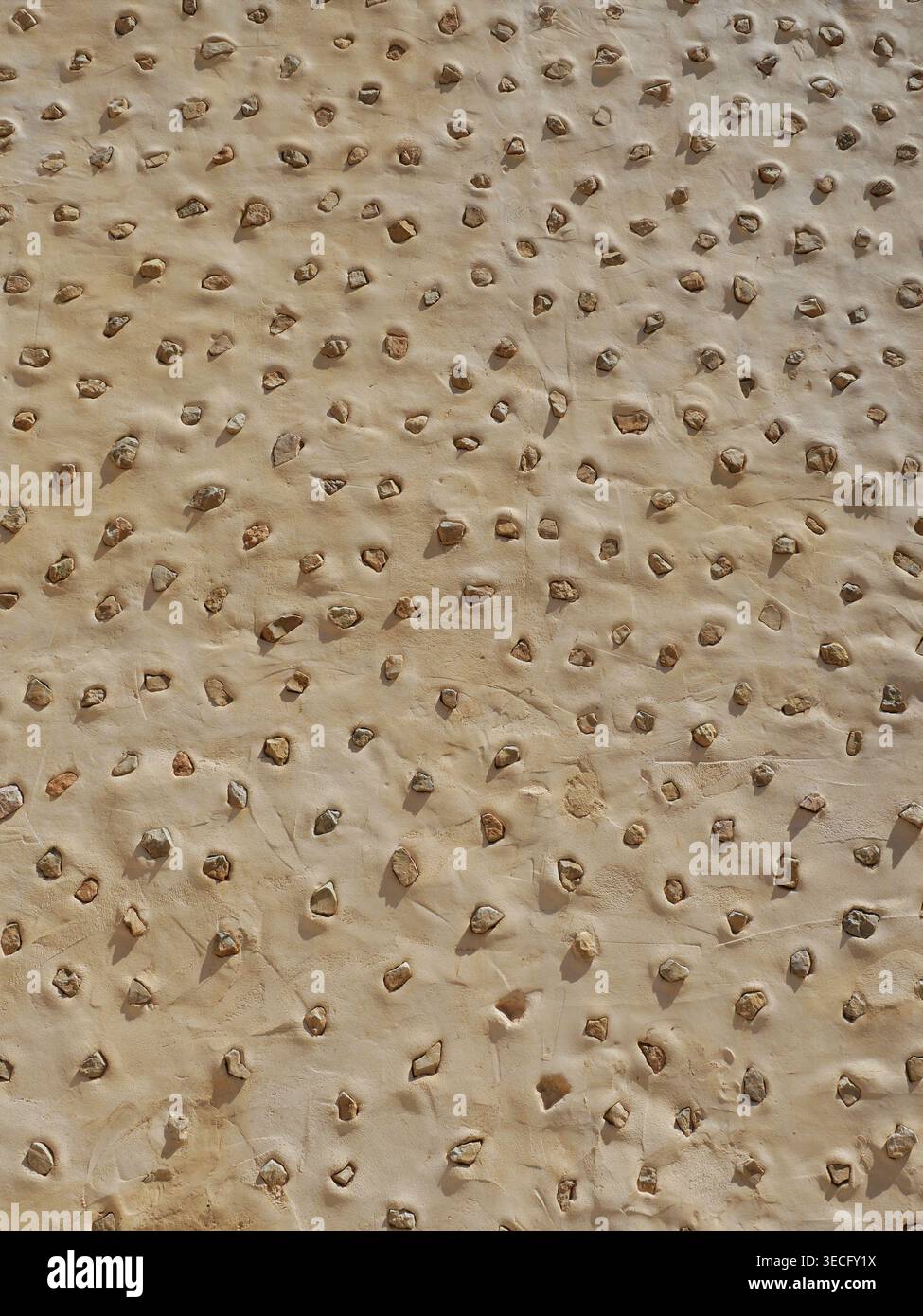 Mediterranean wall with embedded stones in plaster – repeating structure, ideal as background texture. Close-up. Copyspace. Stock Photo