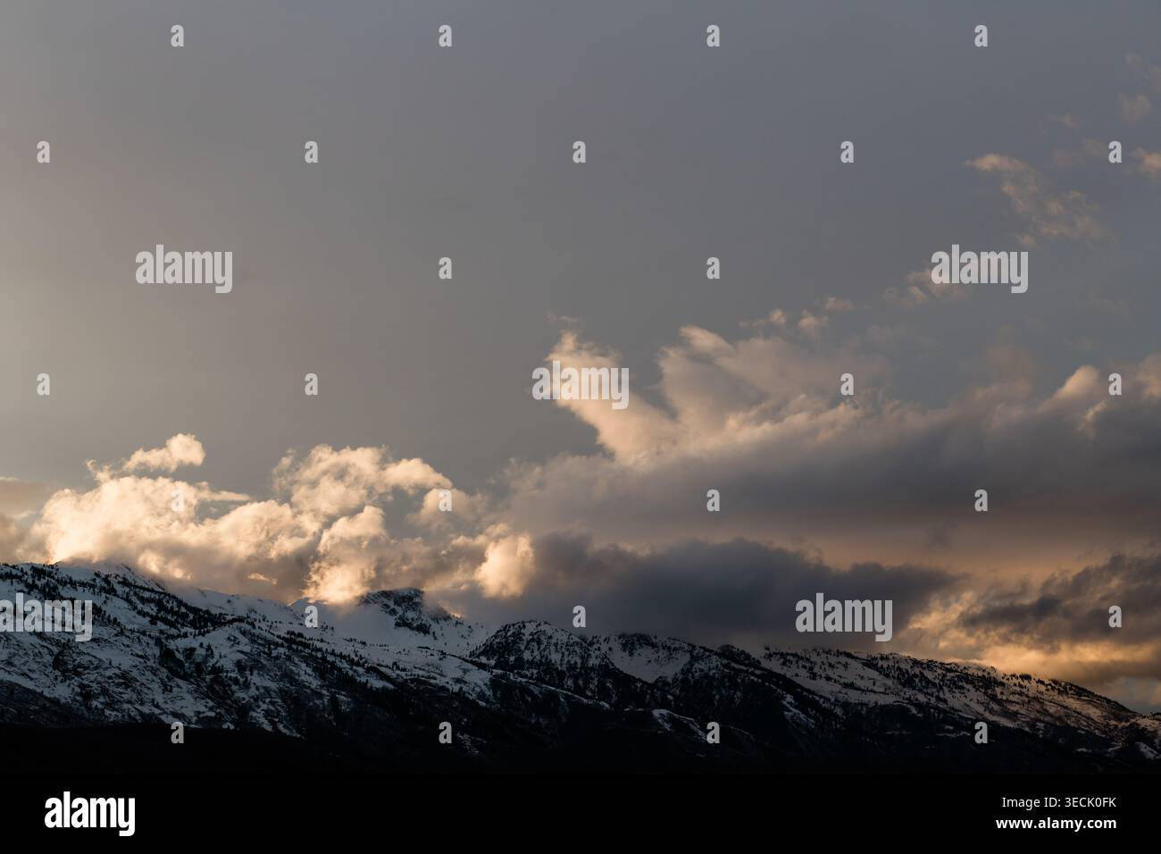 Storm clouds gathering over snowy mountain range at dusk Stock Photo