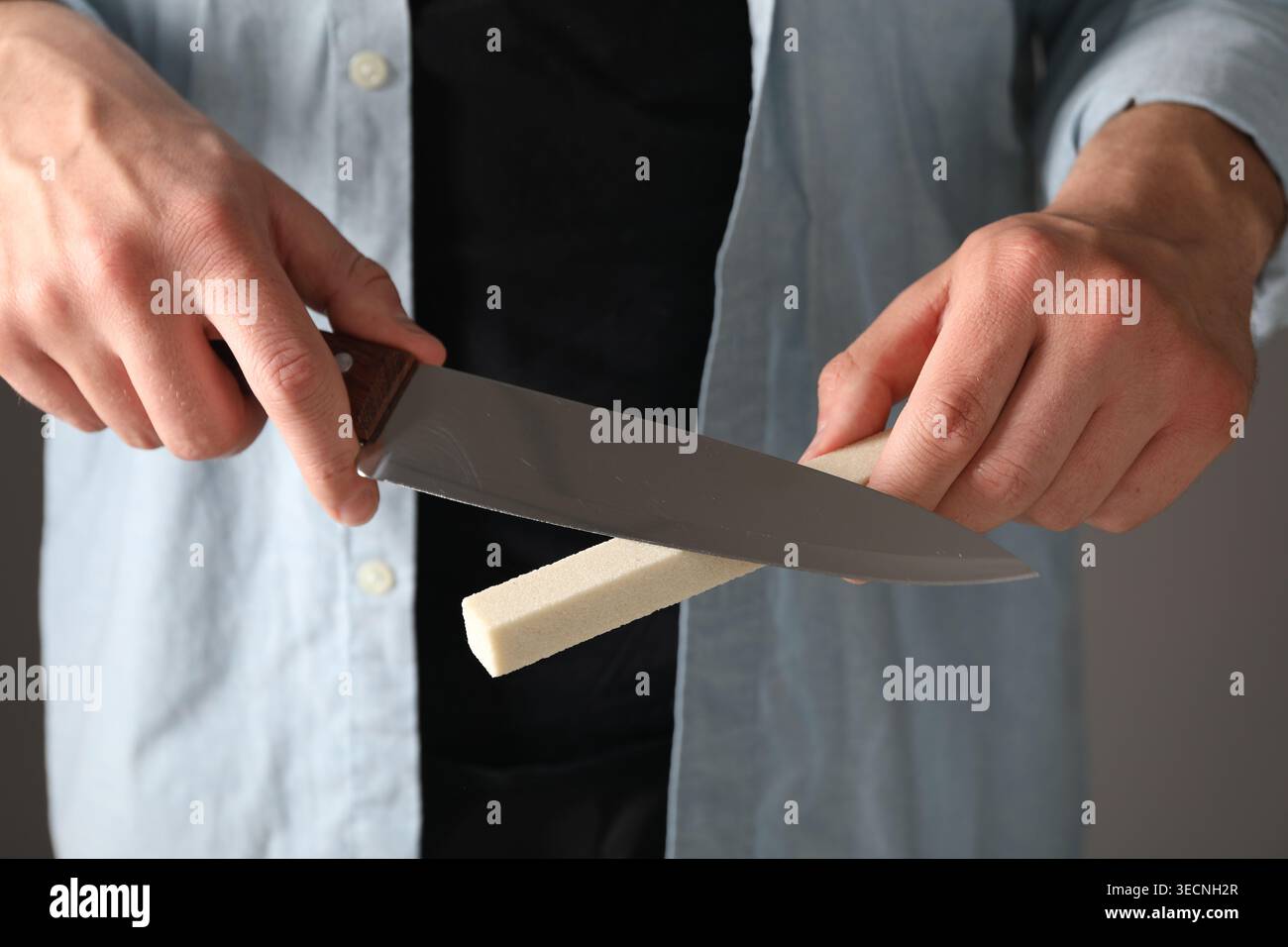 Man sharpening knife on grey background, closeup Stock Photo