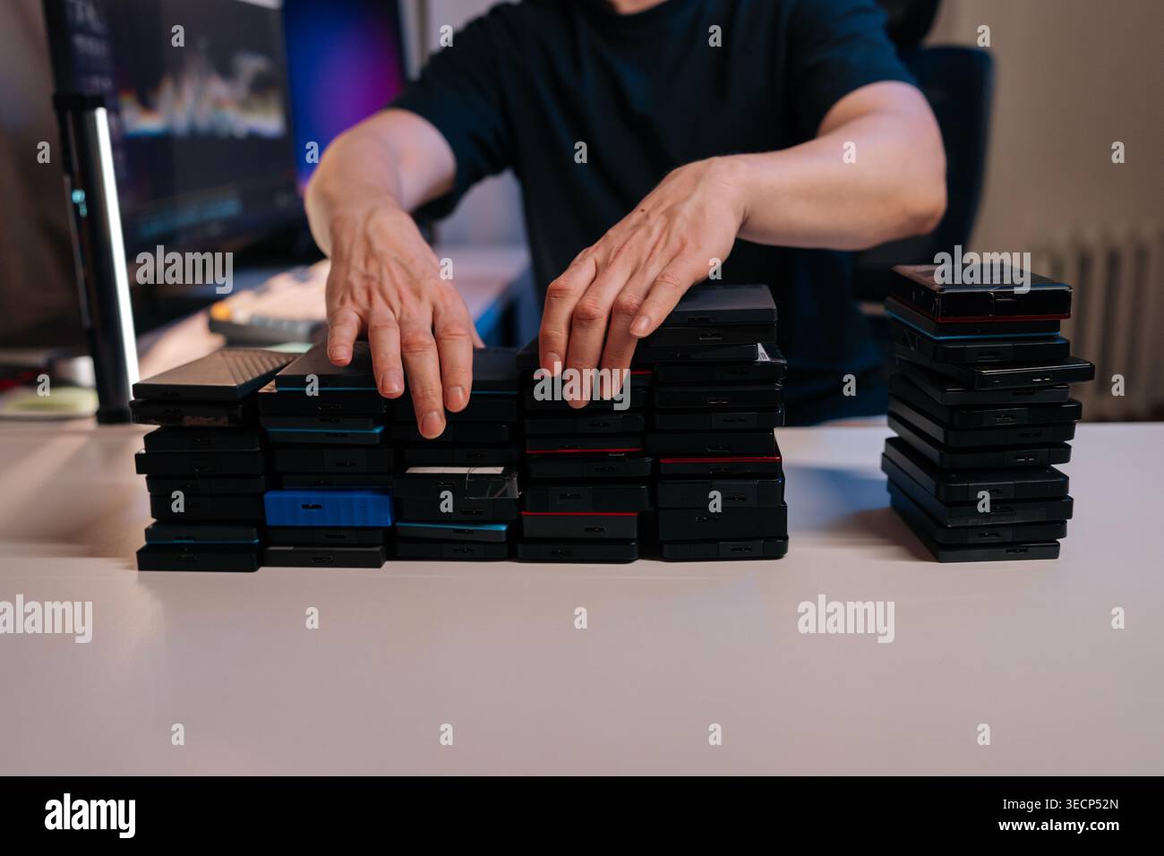 Person stacking multiple external hard drives on desk, creating organized piles for secure data management, archiving, digital asset backup in home Stock Photo