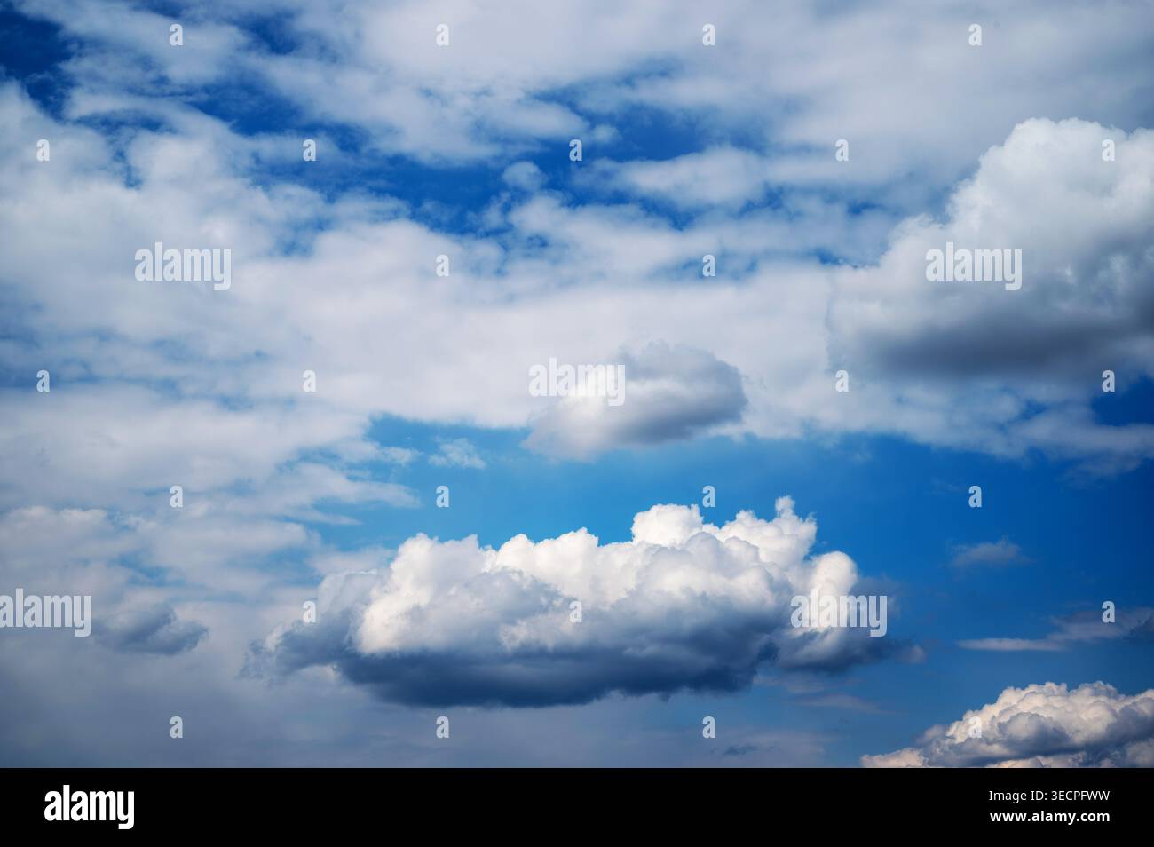 Fluffy white clouds floating across deep blue sky Stock Photo